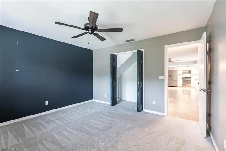 Unfurnished bedroom featuring ceiling fan, light carpet, and stainless steel refrigerator with ice dispenser
