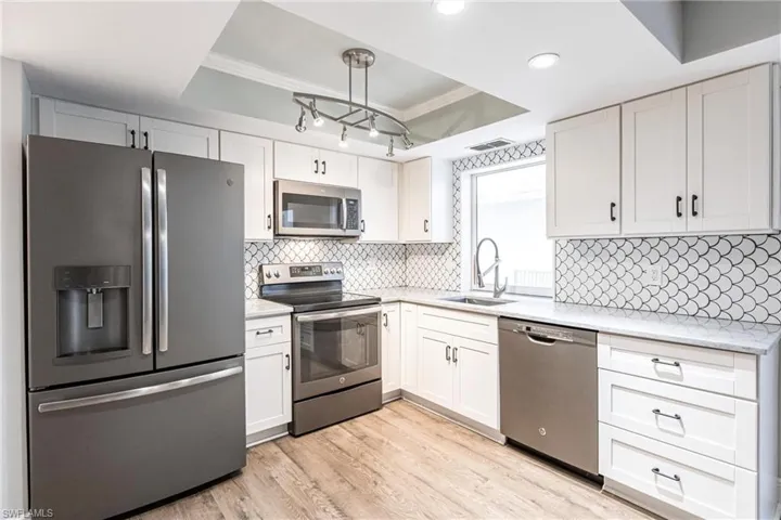 Kitchen with white cabinets, pendant lighting, stainless steel appliances, and a raised ceiling