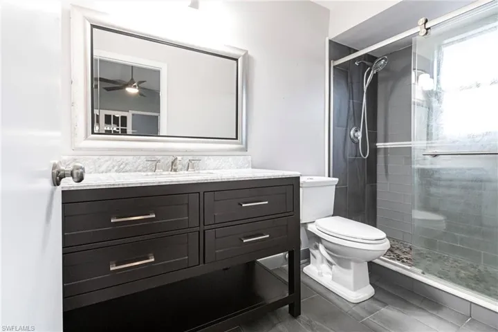 Bathroom featuring ceiling fan, toilet, walk in shower, and vanity