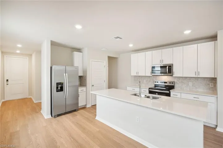 Kitchen with a center island with sink, stainless steel appliances, white cabinetry, light wood-type flooring, and sink
