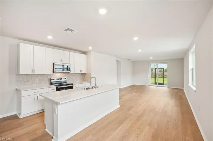 Kitchen with a center island with sink, white cabinets, sink, light wood-type flooring, and appliances with stainless steel finishes