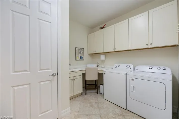 Laundry area with independent washer and dryer, counter with laundry tub, light tile patterned floors, and cabinet space
