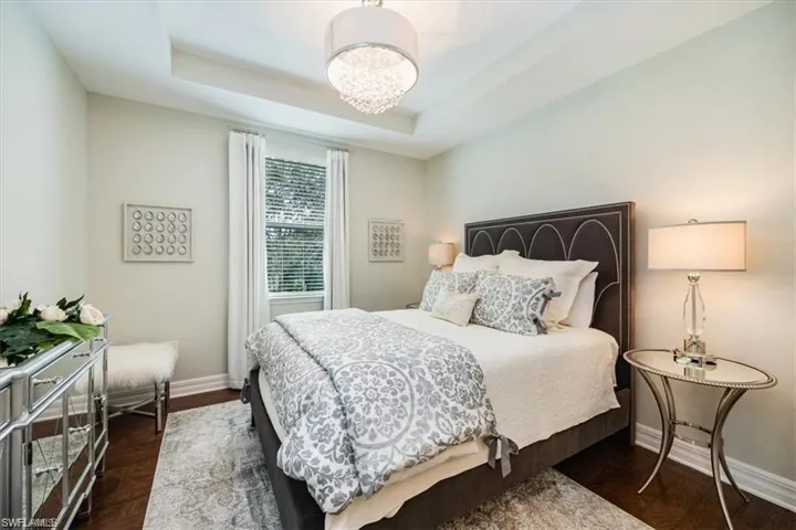Den featuring a raised ceiling, dark wood-style flooring, and a chandelier