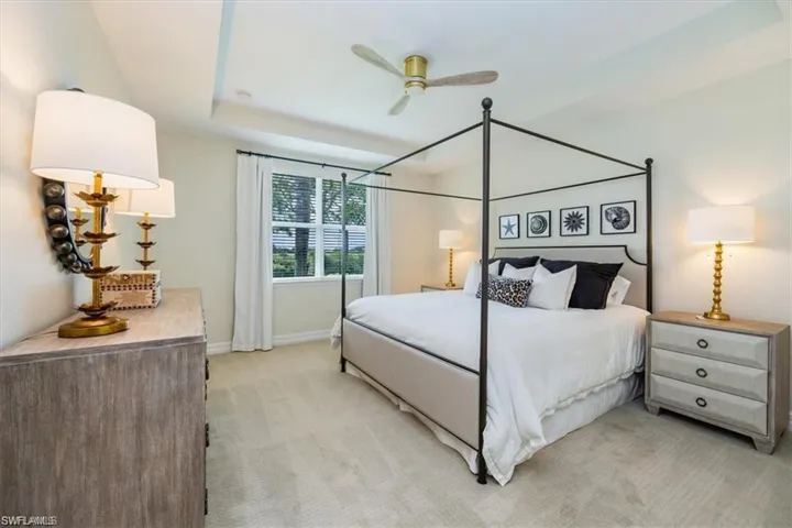 Bedroom with a raised ceiling, light colored carpet, and ceiling fan