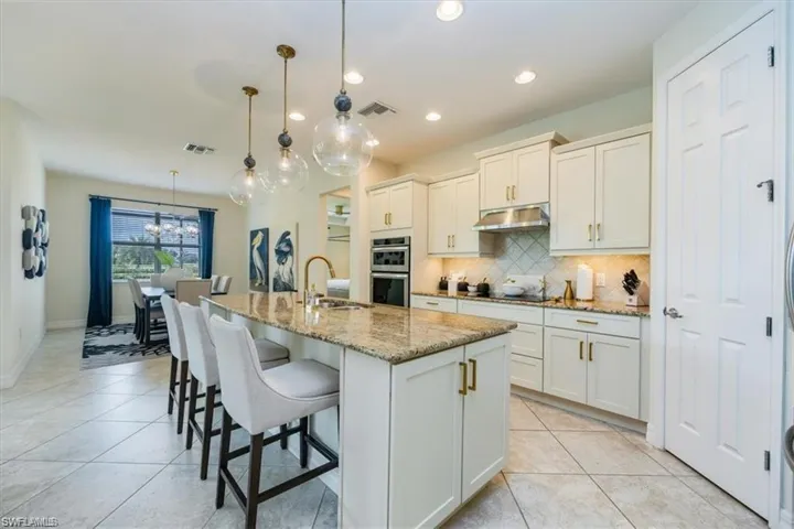 Kitchen featuring tasteful backsplash, light tile patterned floors, decorative light fixtures, light stone counters, and an island with sink