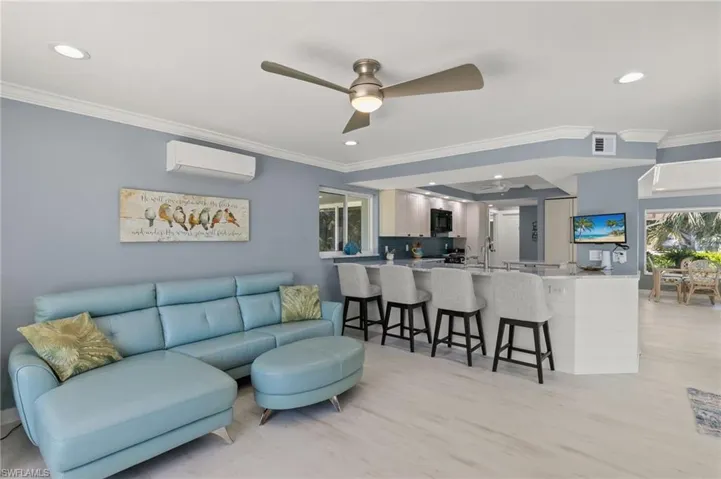 Living area with visible vents, a ceiling fan, a wall mounted AC, crown molding, and light wood finished floors