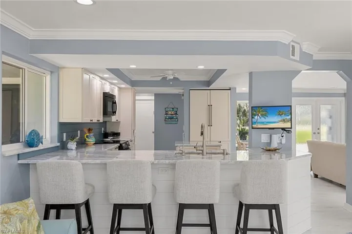 Kitchen with a peninsula, light stone countertops, black microwave, and a sink