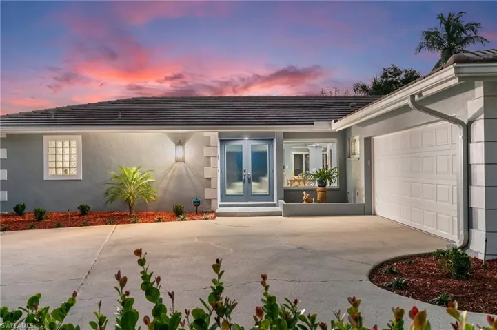 Exterior entry at dusk with stucco siding, french doors, concrete driveway, an attached garage, and a tiled roof