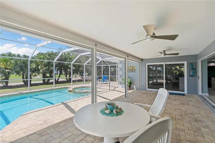 View of pool featuring glass enclosure, a patio area, a pool with connected hot tub, and ceiling fan