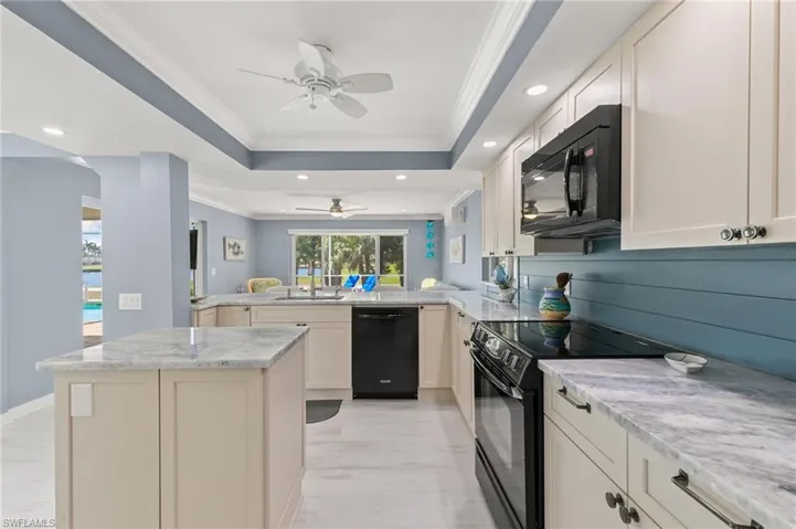 Kitchen featuring black appliances, a ceiling fan, a peninsula, crown molding, and a raised ceiling