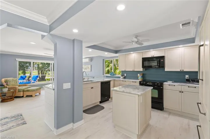 Kitchen with visible vents, a center island, ornamental molding, light stone counters, and black appliances
