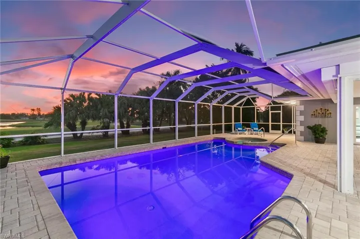 Pool at dusk with a patio area, glass enclosure, and a pool with connected hot tub
