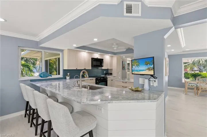 Kitchen with visible vents, crown molding, black microwave, light stone counters, and a sink