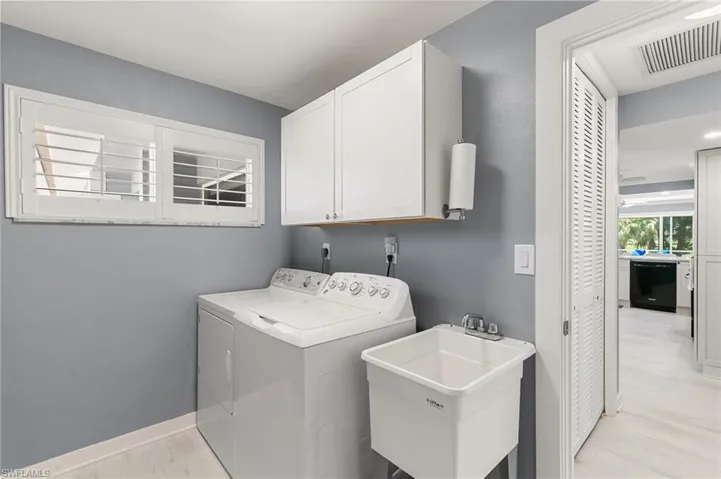 Laundry room with washing machine and clothes dryer, visible vents, light wood-type flooring, cabinet space, and a sink