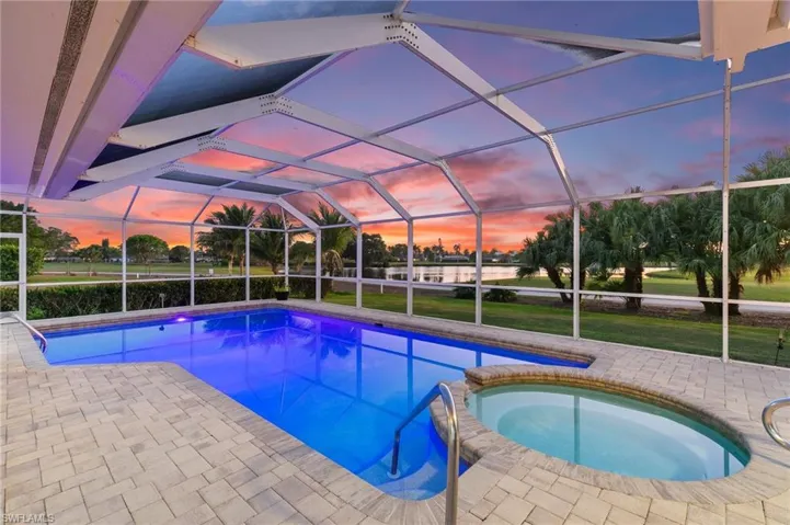 Pool at dusk with a lanai, a pool with connected hot tub, and a patio