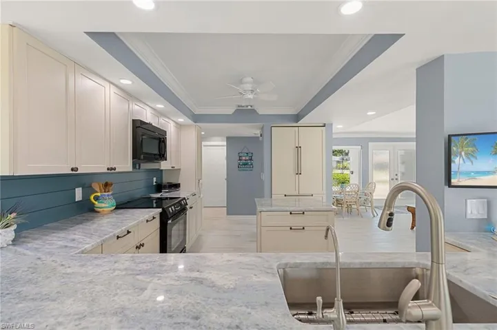 Kitchen featuring crown molding, light stone countertops, black appliances, a raised ceiling, and a sink