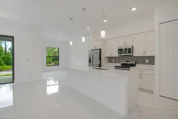 Kitchen with plenty of natural light, a kitchen island with sink, light tile flooring, and appliances with stainless steel finishes