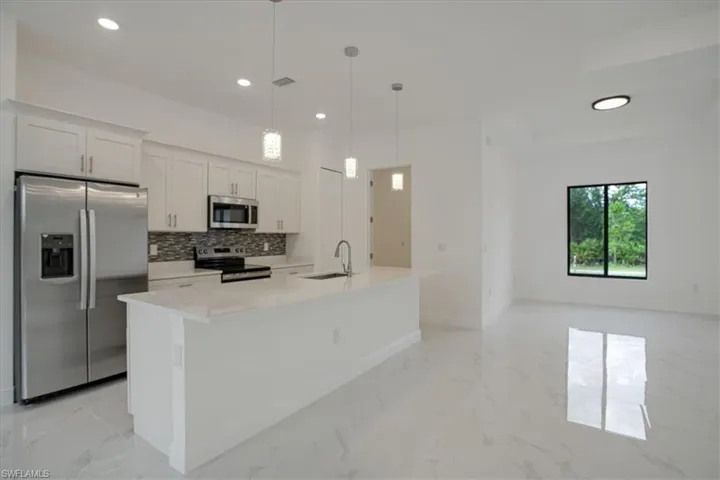 Kitchen featuring an island with sink, decorative light fixtures, light tile flooring, sink, and appliances with stainless steel finishes