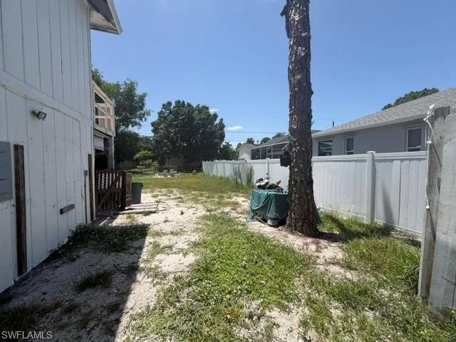 Spacious yard featuring a privacy fence, mature tree, and a two-story structure with an upper-level balcony