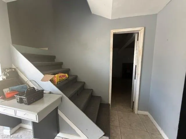 Carpeted staircase with light gray walls, white baseboards, and a tiled floor