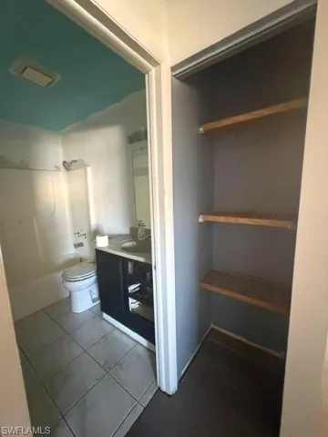 Bathroom featuring a white toilet, dark vanity with undermount sink, and tiled flooring
