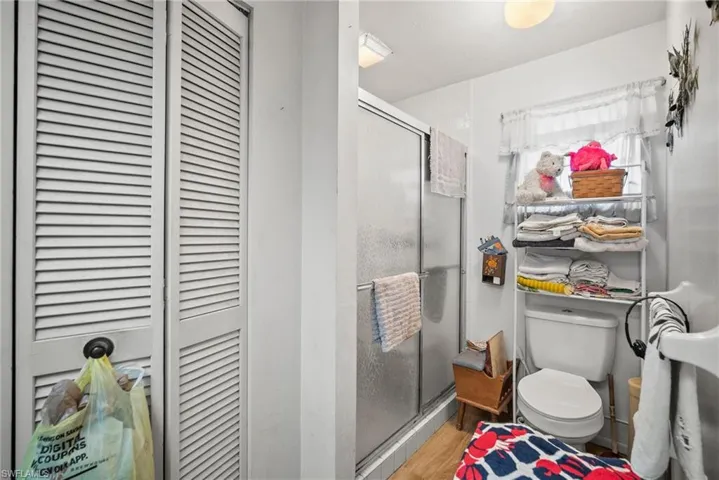 Bathroom featuring a closet, toilet, a stall shower, and wood finished floors