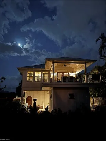 Back of house at night featuring a ceiling fan and a balcony