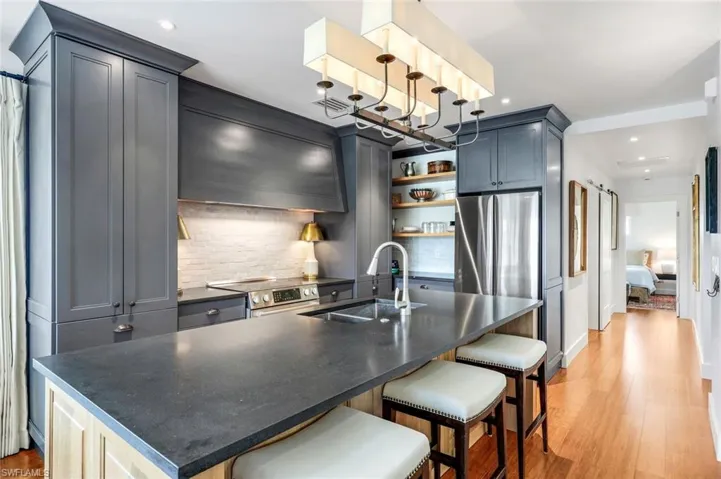 Kitchen featuring dark countertops, wall chimney range hood, light wood-style flooring, stainless steel appliances, and a sink