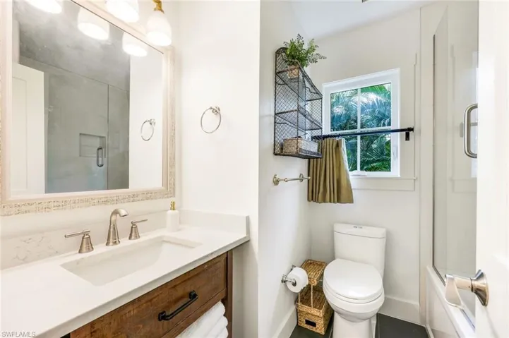 Bathroom featuring baseboards, toilet, vanity, and bath / shower combo with glass door