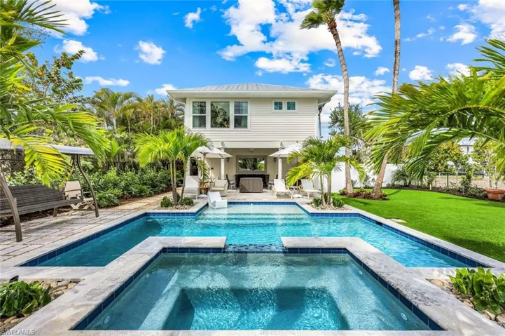 Rear view of house featuring fence, a lawn, a pool with connected hot tub, and a patio area