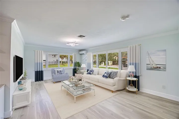 Living room featuring a wall unit AC, visible vents, baseboards, ornamental molding, and light wood-type flooring