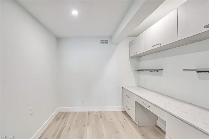 Unfurnished office with built in desk, light wood-type flooring, visible vents, and baseboards