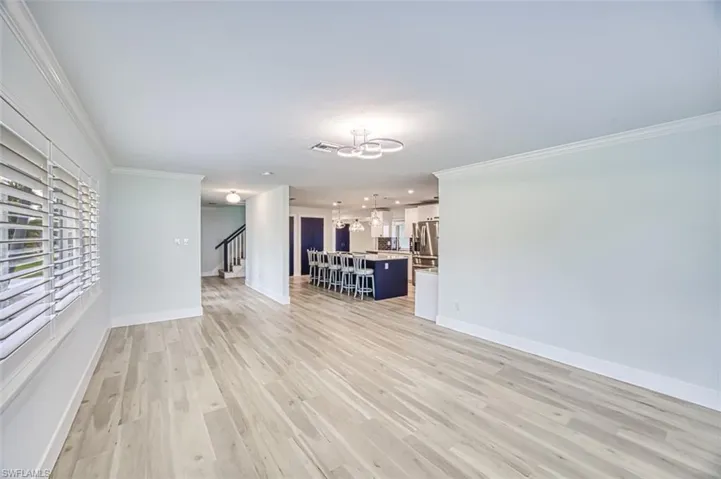 Unfurnished living room featuring stairs, ornamental molding, light wood-type flooring, and a chandelier