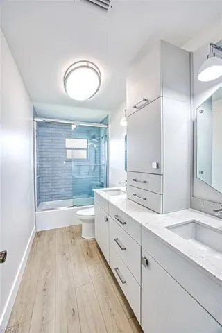 Bathroom with shower / bath combination with glass door, a sink, toilet, and wood finished floors