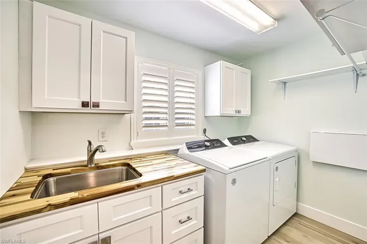 Washroom featuring cabinet space, baseboards, light wood-style floors, washing machine and dryer, and a sink