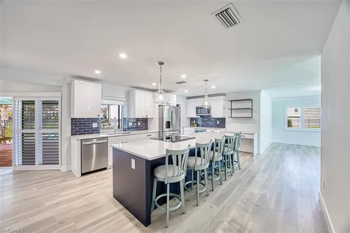 Kitchen featuring visible vents, appliances with stainless steel finishes, a kitchen island with sink, a sink, and a kitchen bar