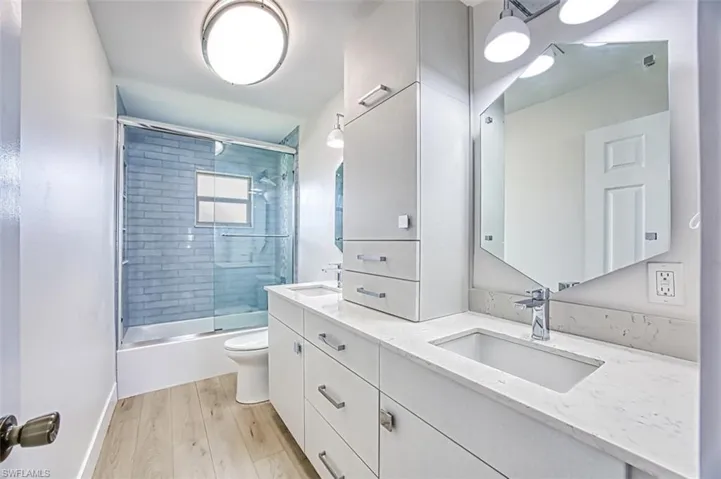 Full bath featuring enclosed tub / shower combo, a sink, toilet, and wood finished floors