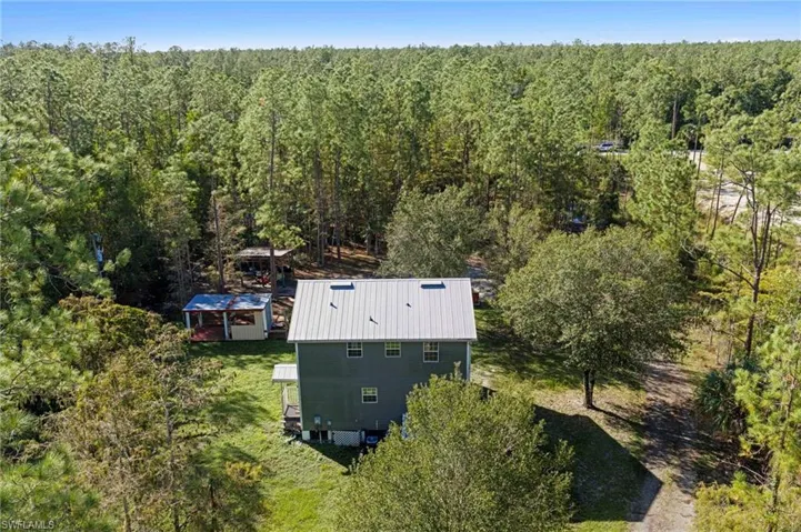 Two-story residence featuring a metal roof, skylights, exterior wood siding, and detached covered structures, situated on a lot surrounded by mature trees