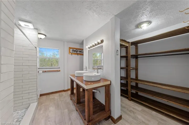 Custom wood-frame vanity featuring dual vessel sinks and a flat-surface countertop, walk-in closet with built-in wooden shelving, wood-finish tile flooring, and a tiled walk-in shower