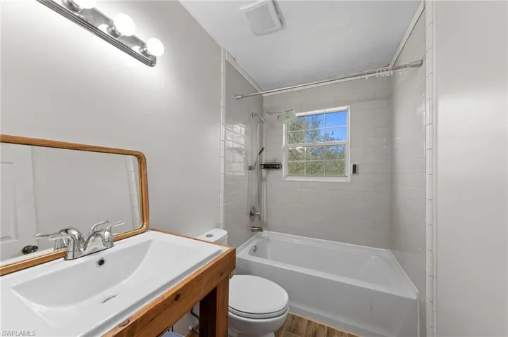 Bathroom featuring a custom wood-framed vanity, white basin, subway-tiled shower surround with integrated hardware, and wood-finish flooring
