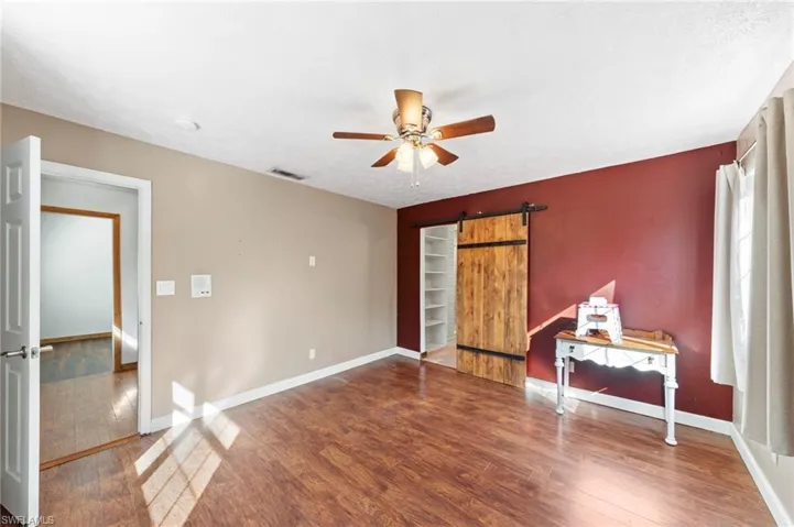 Room featuring wood-finish flooring, a ceiling fan with integrated lighting, a sliding wood barn-style door, and built-in shelving