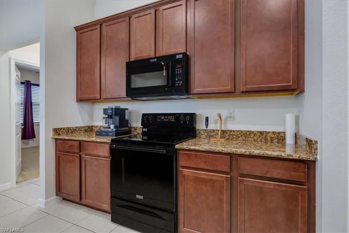 Kitchen featuring black appliances, light stone counters, light tile patterned floors, and brown cabinetry