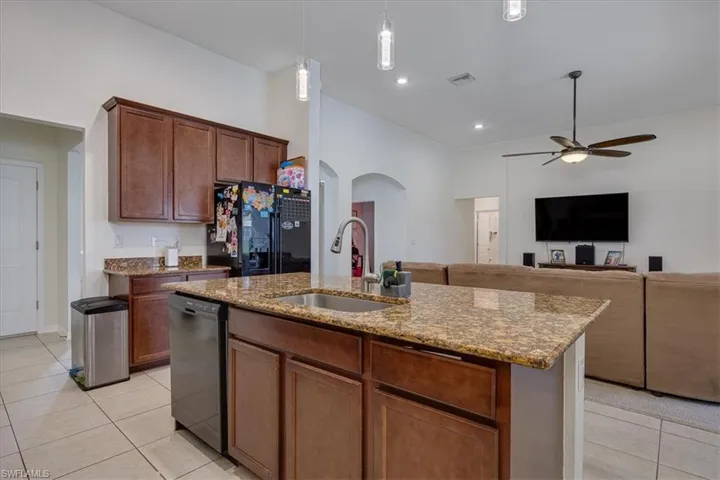 Kitchen featuring light tile patterned flooring, ceiling fan, arched walkways, black appliances, and open floor plan
