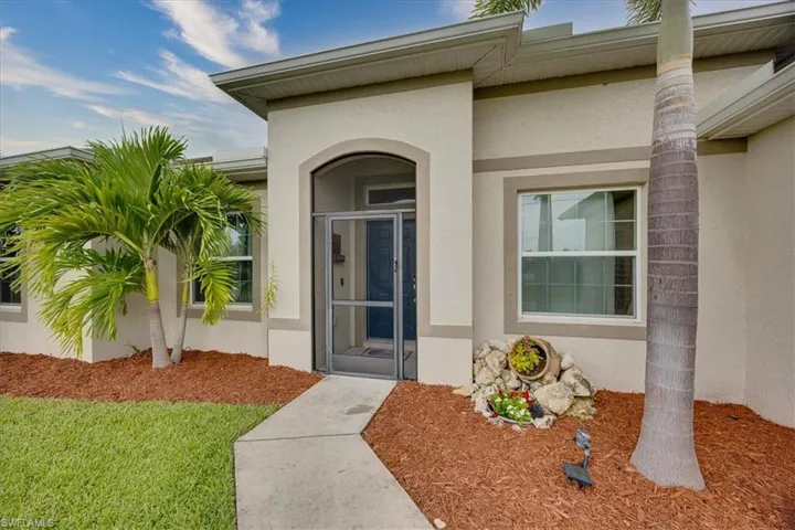 View of exterior entry with stucco siding and a yard