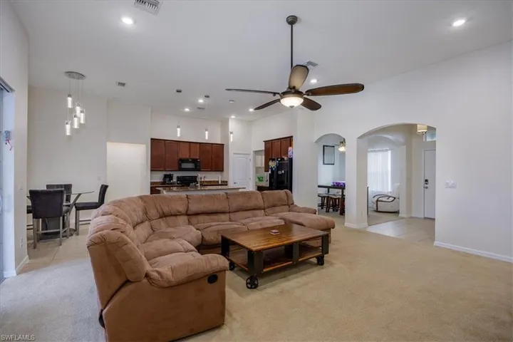 Living room with a ceiling fan, light carpet, arched walkways, recessed lighting, and a towering ceiling