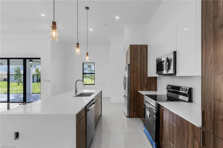 Kitchen featuring white cabinetry, a large island, hanging light fixtures, appliances with stainless steel finishes, and sink