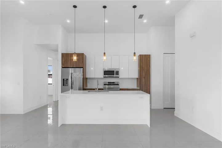 Kitchen featuring light tile patterned flooring, white cabinets, an island with sink, hanging light fixtures, and appliances with stainless steel finishes
