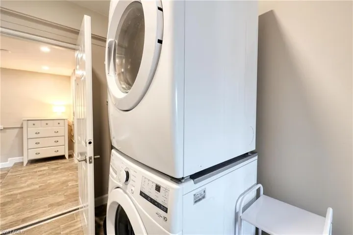 Clothes washing area with stacked washer and clothes dryer, recessed lighting, baseboards, light wood-style flooring, and laundry area