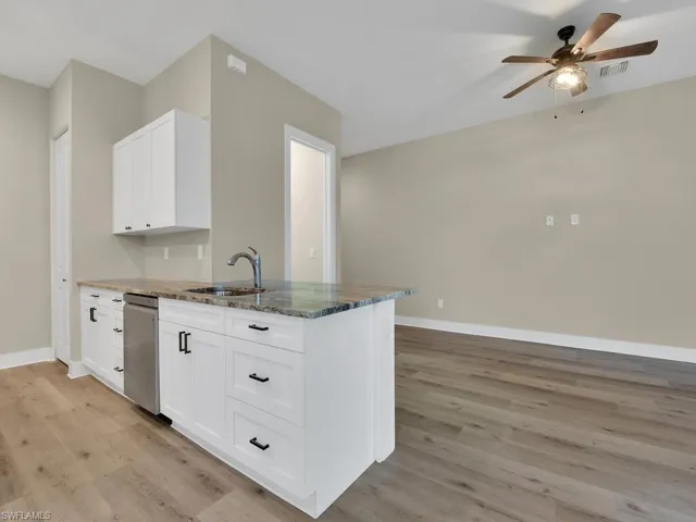 Kitchen with light hardwood / wood-style floors, white cabinets, dark stone counters, sink, and ceiling fan