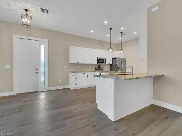 Kitchen featuring light stone countertops, kitchen peninsula, stainless steel appliances, wood-type flooring, and hanging light fixtures